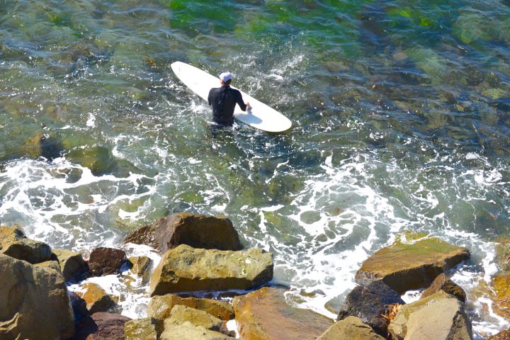 surfer in the water below large rocks